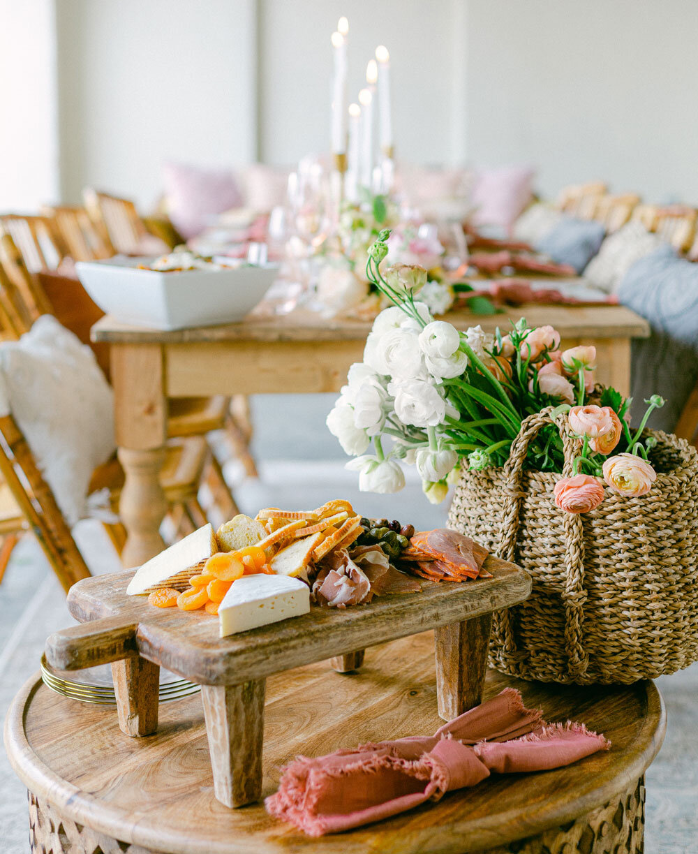 Wedding table featuring an artisanal cheese board adorned with white and light pink flowers, showcasing Joel Catering's expertise in rustic-themed events in New Orleans