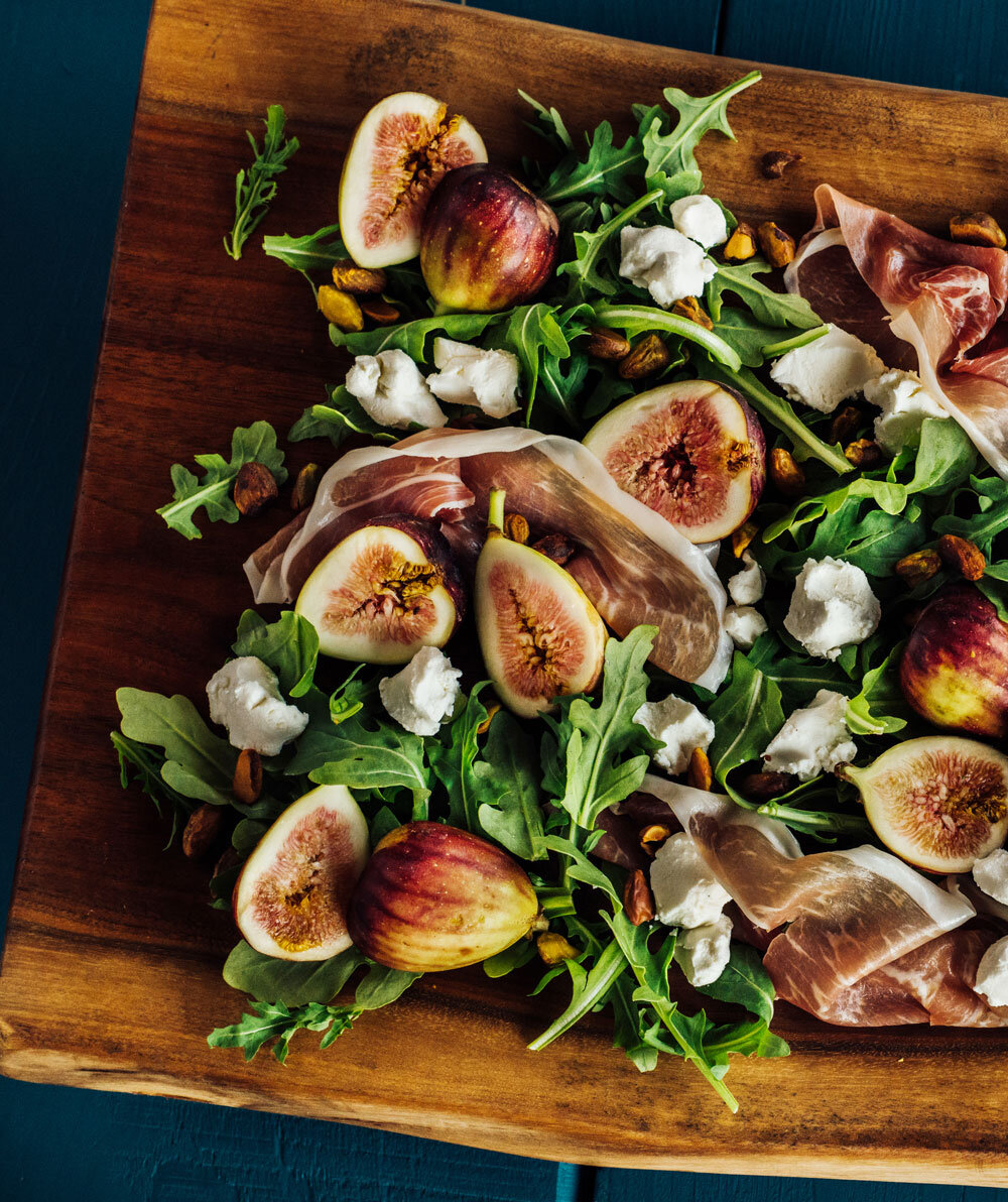 Artfully crafted fig salad with arugula, goat cheese, pistachios, and prosciutto, served on a wooden board, a premium salad dish by Joel Catering in New Orleans.
