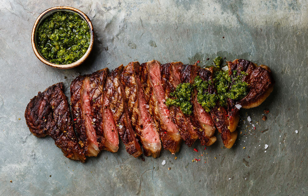 Luxurious chargrilled prime flank steak adorned with fresh chimichurri, presented on a stone slate platter, a testament to Joel Catering's premium culinary offerings in New Orleans.