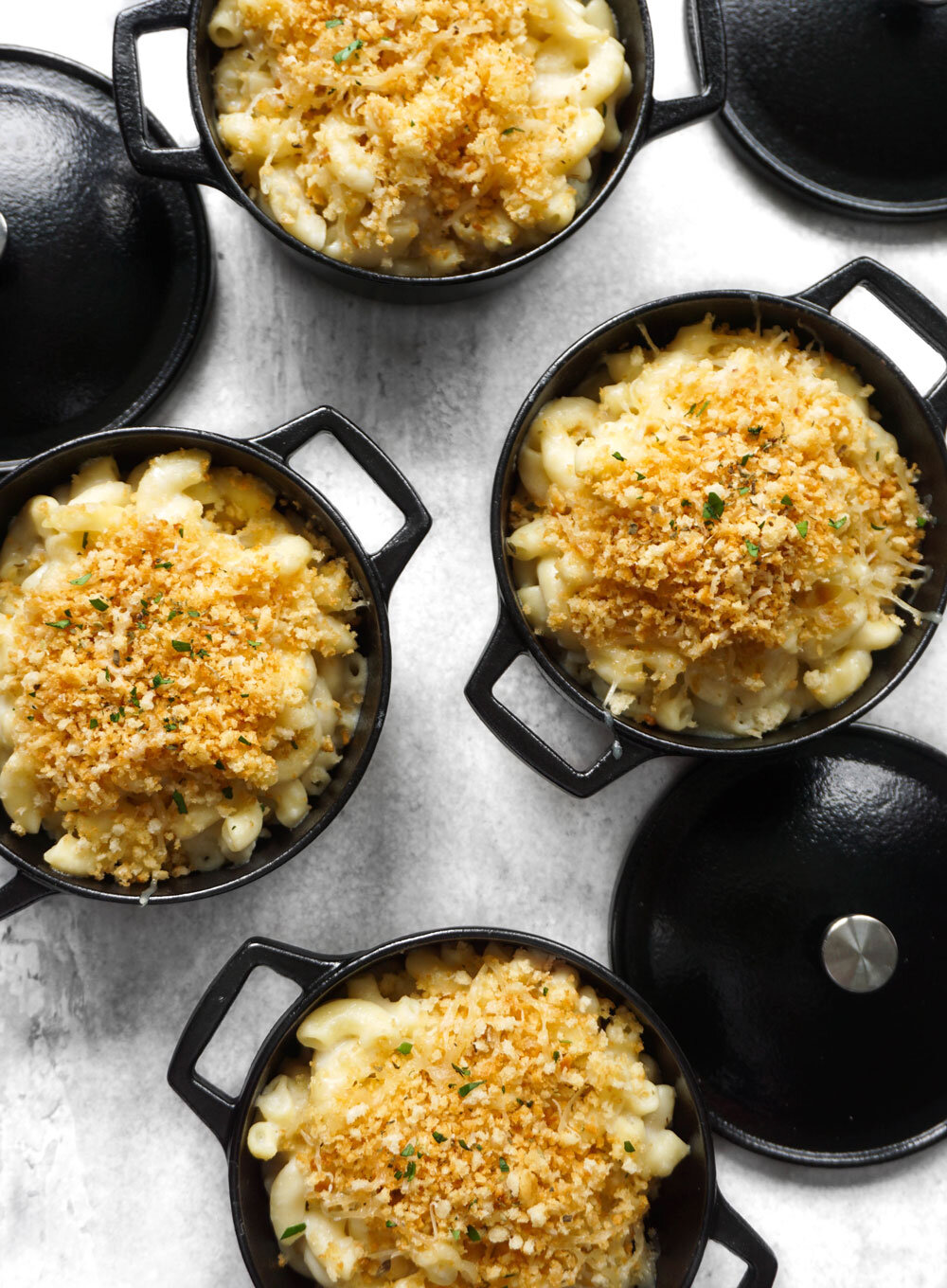 Flat lay of individual truffle mac and cheese servings in cast iron bowls, garnished with fresh breadcrumbs, lemon zest, and parsley, a luxurious dish by Joel Catering in New Orleans.