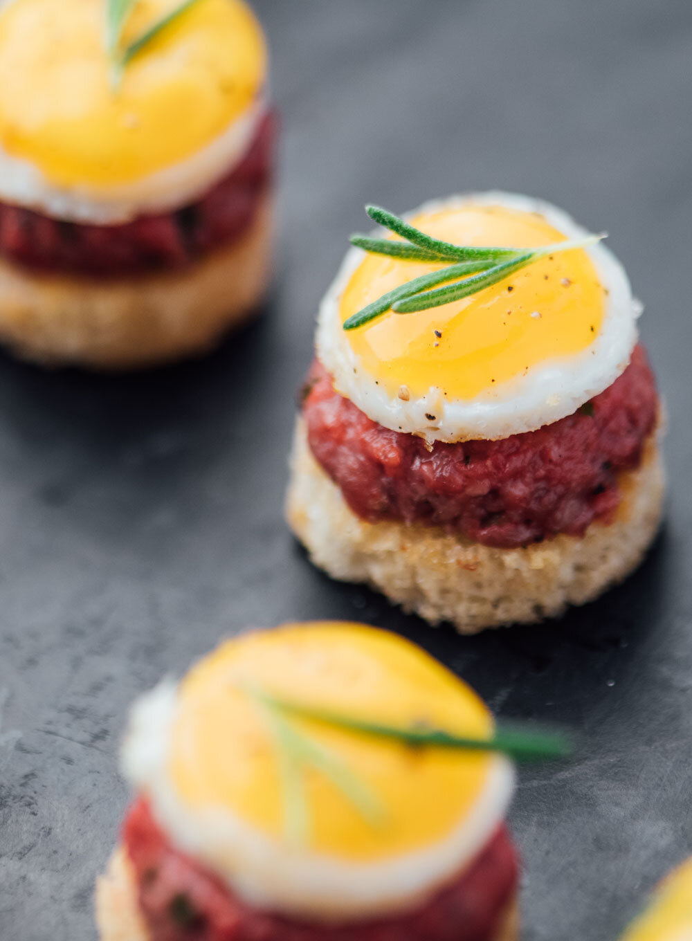 Luxurious round toast bases with Wagyu tartar, quail egg, and rosemary, a premium passed appetizer by Joel Catering, New Orleans' top caterer.